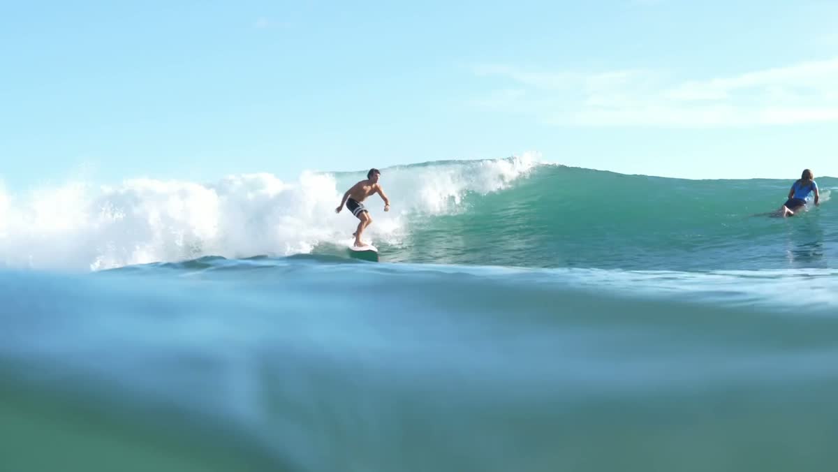 A surfer rides a bright blue wave shot from water level.